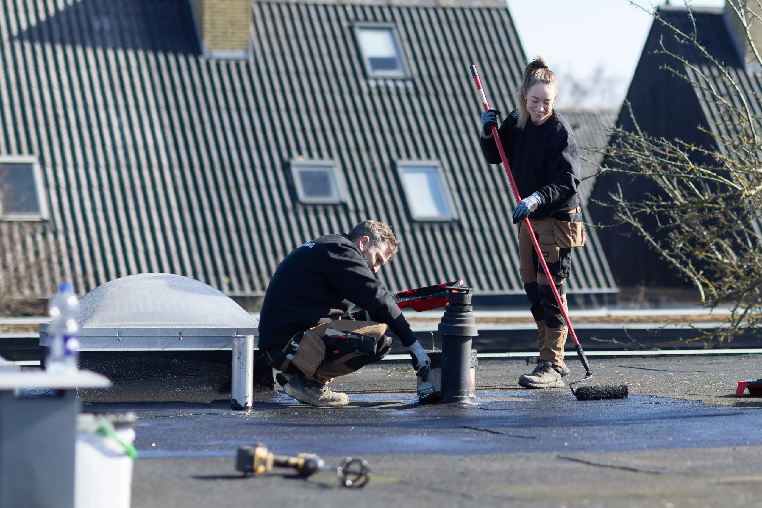To håndværkere arbejder med klimacoating ved ventilationsrør på fladt tag