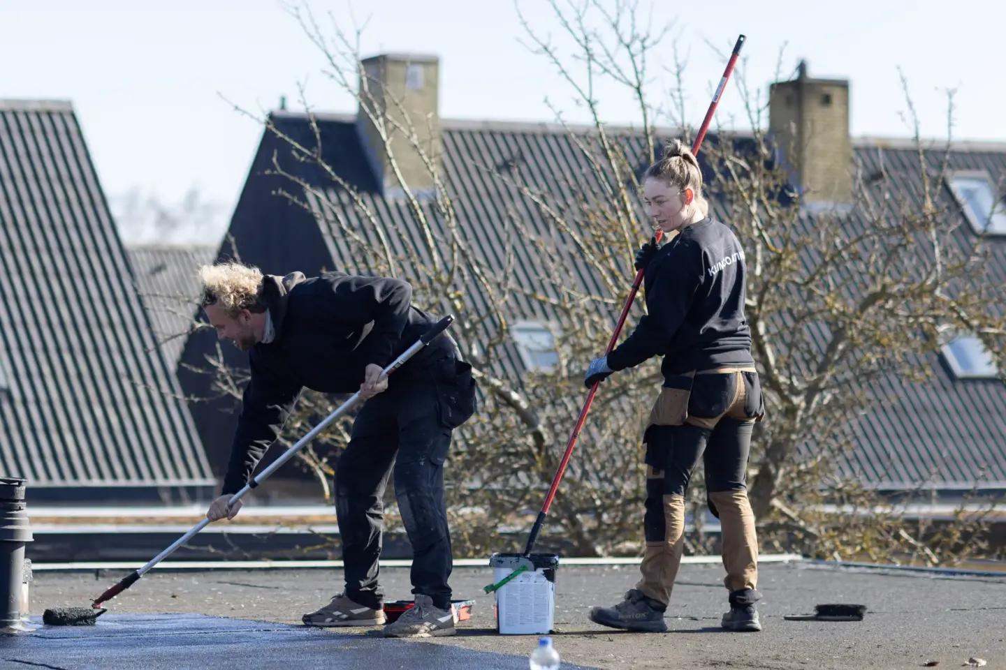 To håndværkere arbejder med klimacoating på fladt tag