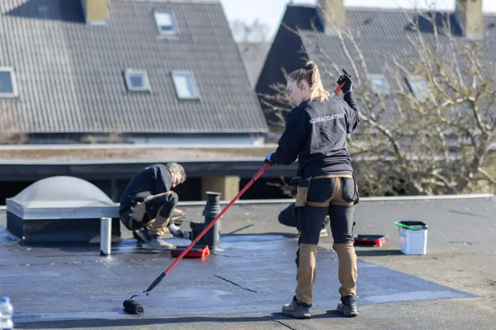 To håndværkere påfører klimacoating på fladt tag med rulle